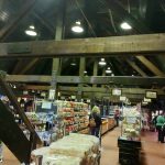 Interior view of a large market with wooden beams, shelves stocked with food, and shoppers.