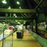 Interior view of a large, industrial-style market aisle with stacked goods and overhead lighting.