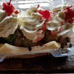 Dessert in clear plastic container topped with whipped cream and red fruit.