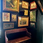 Gallery wall of framed landscape paintings above a rustic wooden bench.