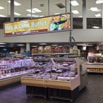 Grocery store interior showing a hot and cold buffet display with fresh food selections.