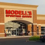 Modell's Sporting Goods store exterior with large windows and brick facade on a sunny day.