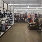 Retail store interior with clothing racks, shelves stocked with merchandise, and a wide aisle.
