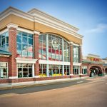 Large tan and brick commercial building with large windows, featuring American flag decor on the facade.