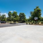 Empty concrete basketball court with surrounding trees and blue sky.