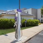 EV charging station in a sunny parking lot near modern commercial buildings.