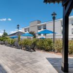 Outdoor patio area with pavers, landscaping, and modern building under a blue sky.