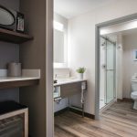 Modern hotel room interior showing a kitchenette area and an open view into a bright bathroom.