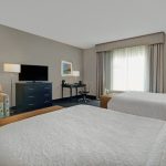 Modern hotel room with large white bed, armchair, and television.