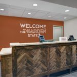 Hotel reception desk with wood paneling, orange accent wall, and "Welcome to the Garden State" sign.