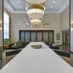 Modern hotel lobby with long white table, contemporary lighting, and seating areas.