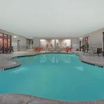Indoor swimming pool with tiled deck, lounge chairs, and large windows overlooking an outdoor area.