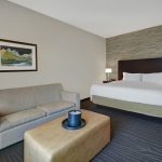 Modern hotel room with beige sofa, king bed, and abstract artwork on the wall.