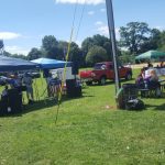 Outdoor community event with music, tents, and inflatable rides on a sunny day.