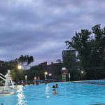 Outdoor swimming pool under a cloudy sky with people swimming and relaxing.