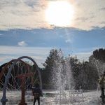 Sunlit water park fountain spray with a Ferris wheel in the background.