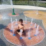 Young boy plays in a circular water fountain area at a playground.