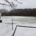 Snow-covered football field with a "Hibernian" sign in the foreground under an overcast sky.
