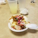 Sweet dessert of ice cream with caramel sauce and rainbow sprinkles in a small white cup.