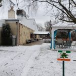 Snowy outdoor scene with a building, trees, and an open-air pavilion.