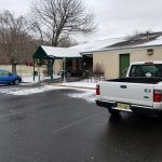 White pickup truck parked near a building with a green awning on a snowy, overcast day.