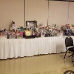 Table display of wrapped holiday gifts and festive items in a large room.