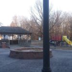Park scene with a gazebo, playground equipment, and bare trees under an overcast sky.