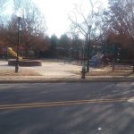 Winter playground scene with swings and slides under bare trees lining a quiet street.