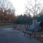 Park playground with colorful equipment under a bright sky, surrounded by trees.