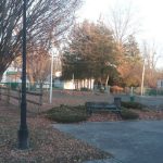 Park scene with trees, benches, and a gazebo under bright daylight.