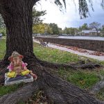Monkey statue resting at the base of a large, old tree near a stone walkway.