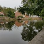 Reflections of buildings and trees in still water under an overcast sky.
