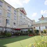 Hilton Garden Inn exterior with a green putting green in the foreground under a blue sky.