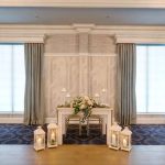 Elegant room with large windows, floral centerpiece on a table, and patterned carpet.