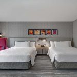Twin hotel beds in a modern room with grey textured wallpaper and artwork.
