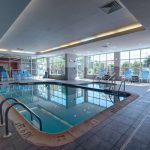 Indoor pool area with blue water, surrounded by tiled deck and large windows.