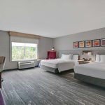 Modern hotel room with two beds, large window view, and neutral decor.