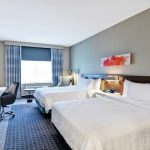 Two white beds in a modern hotel room with gray walls and blue patterned carpet.