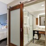 Modern hotel bathroom with glass shower and vanity visible through an open doorway.