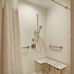 Modern white shower with rainfall head, handheld spray, and built-in bench.