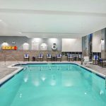 Indoor swimming pool with blue water, lounge chairs, and a modern gray tiled area.