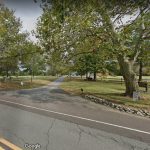 Country road leading into a park with mature trees and grassy fields.