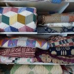Stacked colorful quilted blankets and textiles on white shelves.