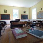 Classroom interior with desks, chalkboard, and educational posters on the walls.