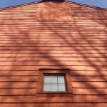 Red wooden siding of a barn with a small window and cupola against a blue sky.