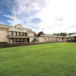 Hotel and conference center building with expansive green lawn under a blue sky.