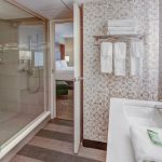 Modern bathroom with glass shower, white tub, and patterned tile accent wall.