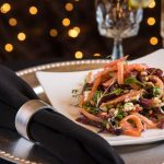 Artisan salad on a white plate, set against a dark background with bokeh lights.
