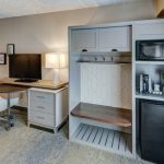 Modern hotel room setup with desk, entertainment center, and built-in mini-fridge.