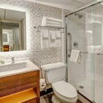 Modern bathroom with wood vanity, white toilet, and glass-enclosed shower.